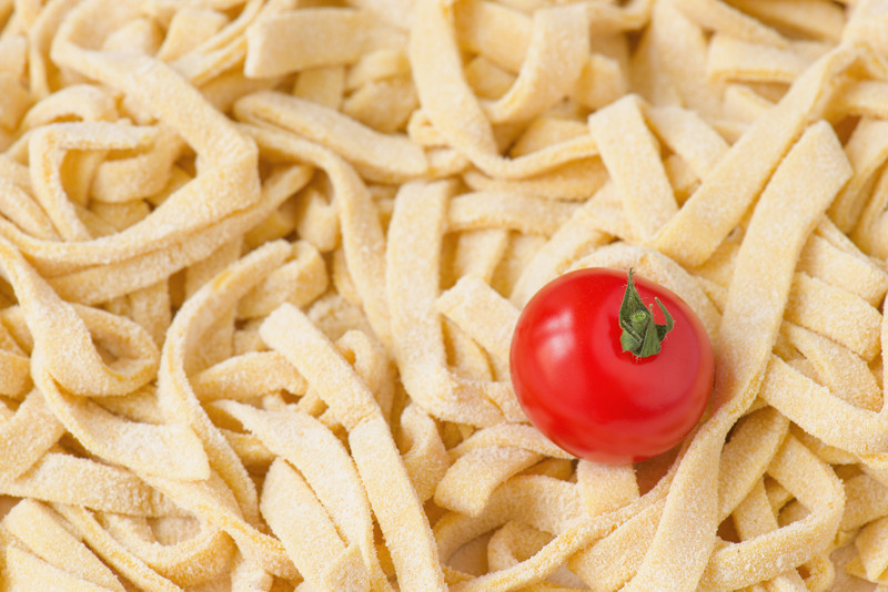 Freshly made tagliatelle, raw, and a single tomato.