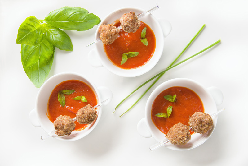 Three bowls filled with tomato sauce, with two meatballs each, on a white background
