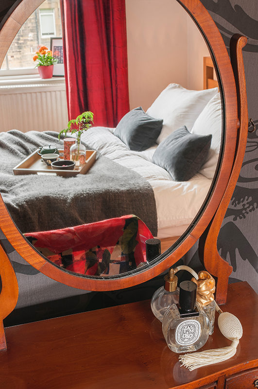Interior design, reflection of bed and tray in mirror with perfume bottle.