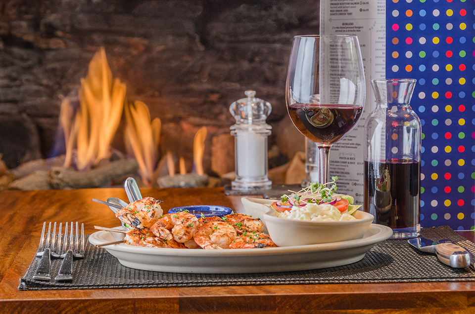 Prawns, sauce, side salad and glass of red wine with fire in background