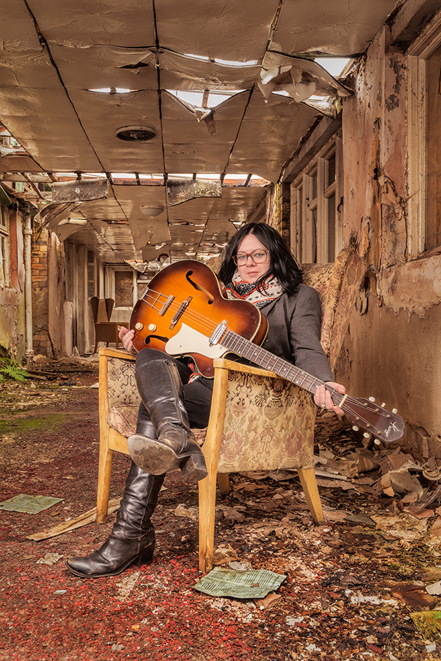 Singer/songwriter Sandra MacBeth sitting in a chair in a derelict location