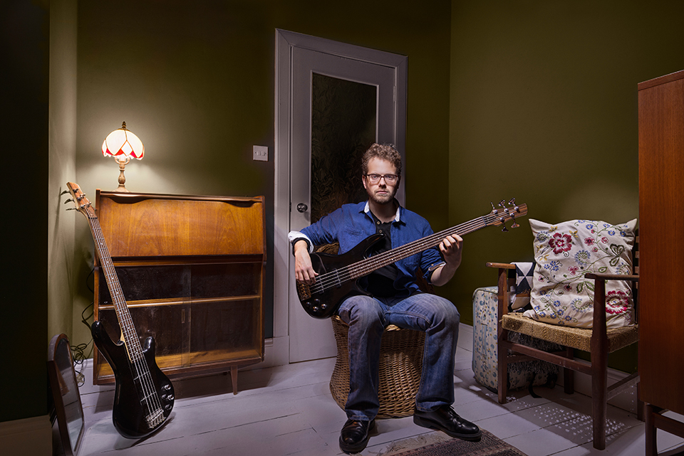 Musician Tom Fairbairn sitting with his bass guitar.