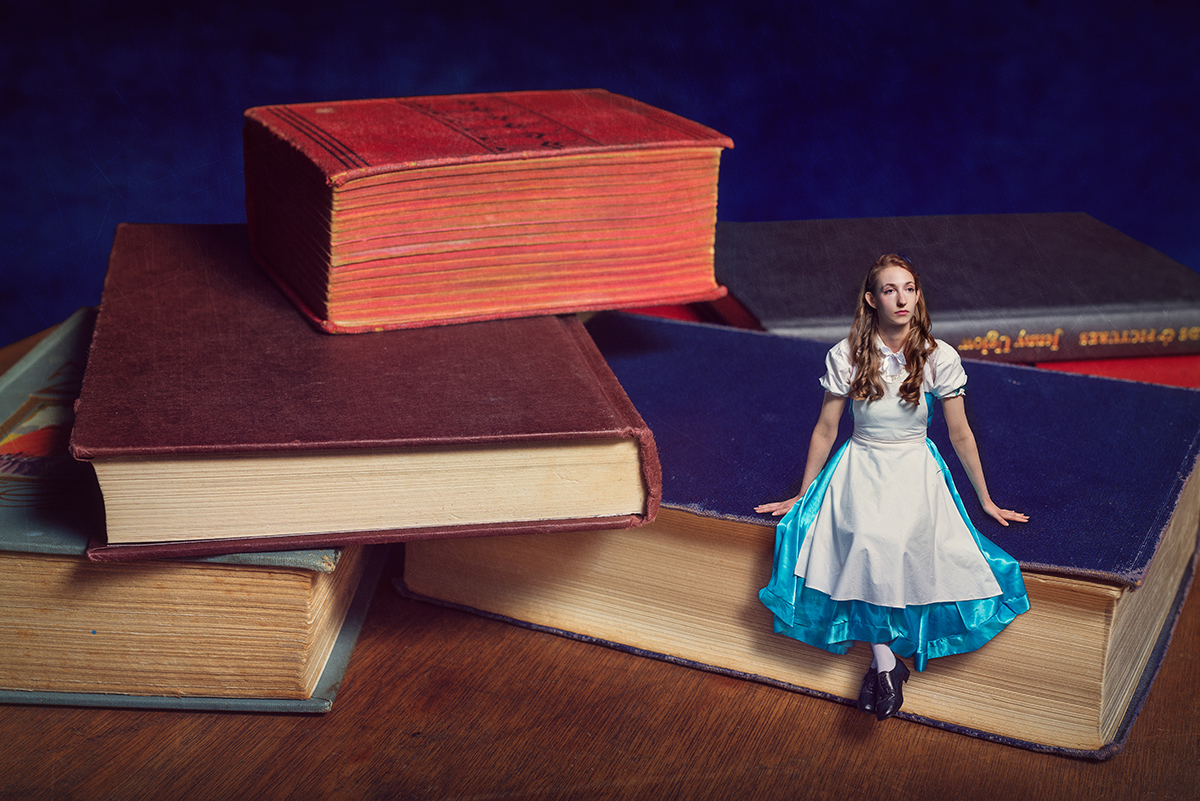 Circus artist Rosella Elphinstone in an Alice in Wonderland costume sitting on a book next to a pile of books