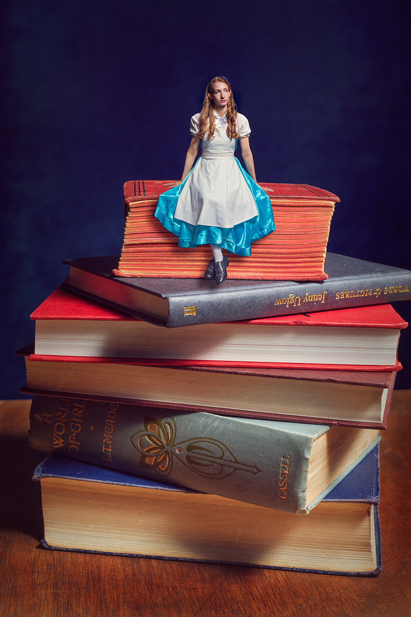 Circus artist Rosella Elphinstone in an Alice in Wonderland costume sitting on a pile of books