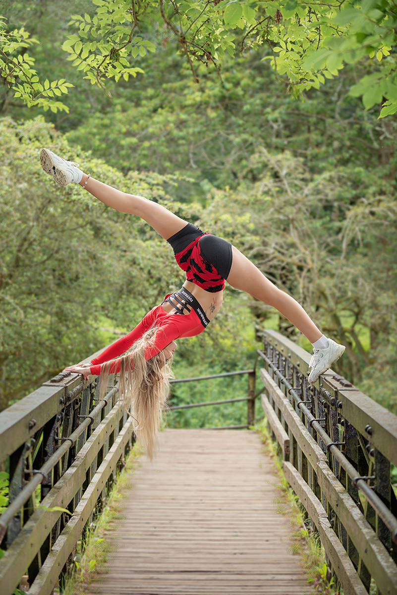 Dancer Holly Wilson doing a vertical split on the rails of a bridge. Vertical image.