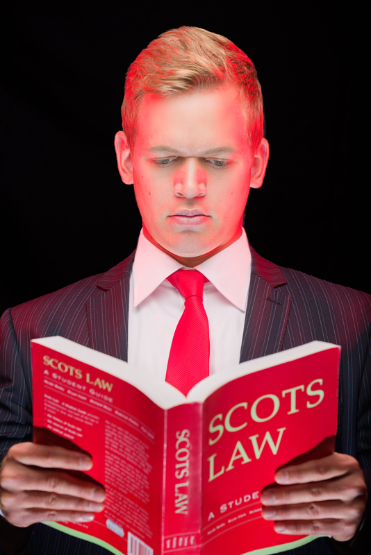Portrait of Mark McLeod of Scotia Accounting against a black background and holding a red 'Scots Law' book. Two of the lights are coloured red.