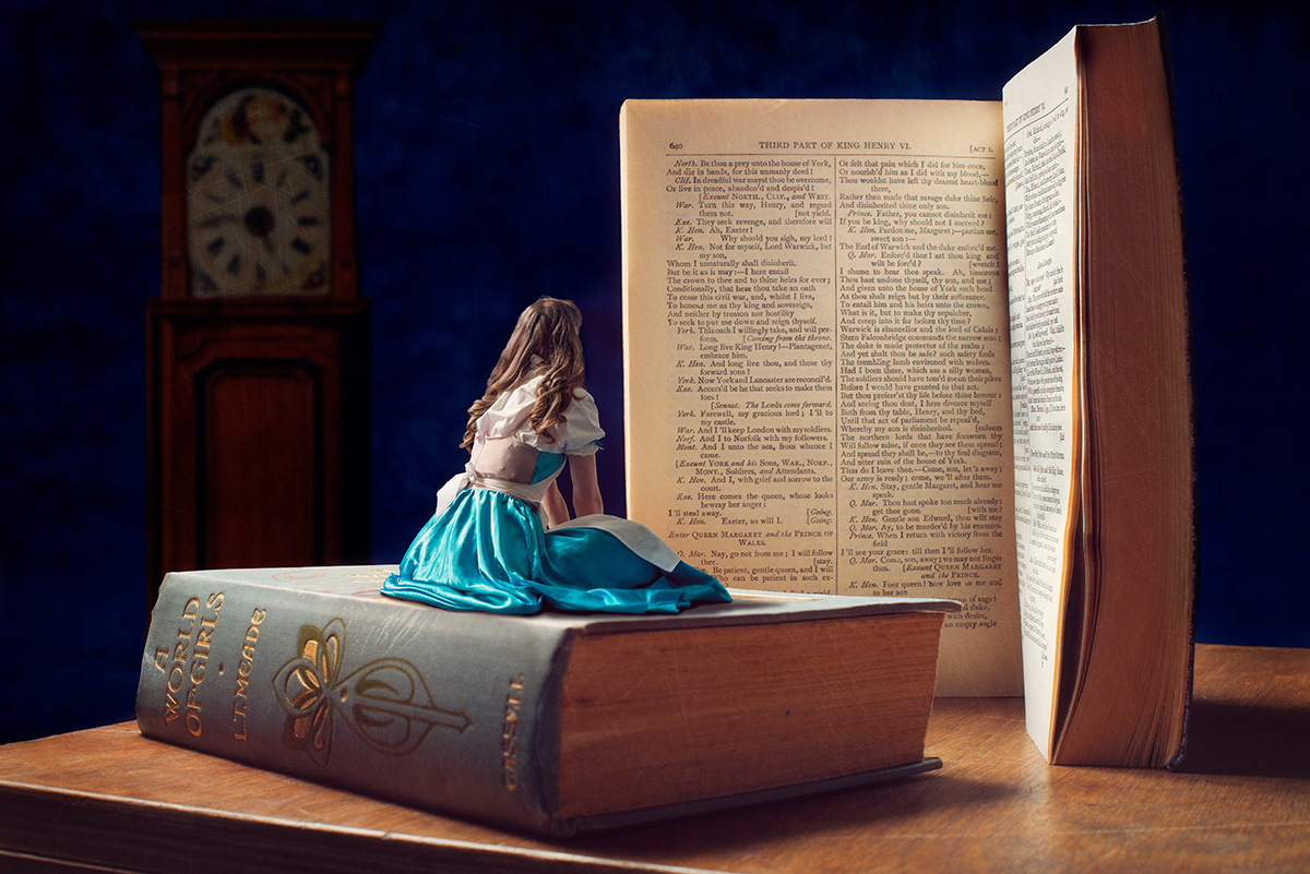 Circus artist Rosella Elphinstone in an Alice in Wonderland costume sitting on a book while reading another.