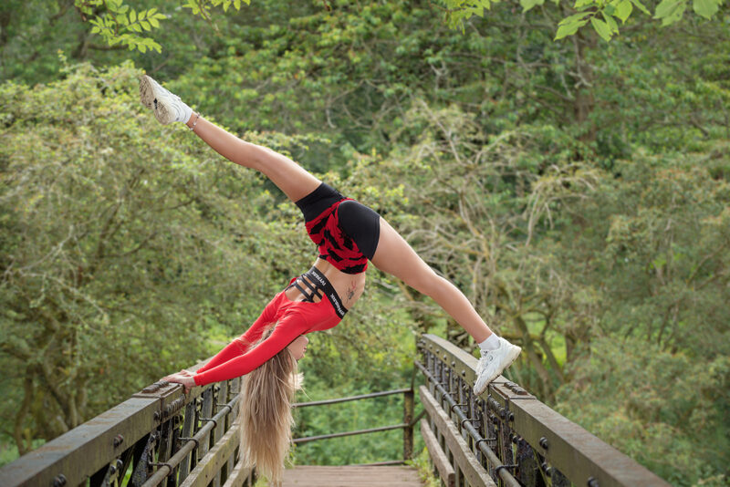 Dancer Holly Wilson doing a vertical split on the rails of a bridge. Horizontal image.